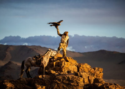 Barzabai, a eagle hunter, with is eagle and horse on rugged cliffs of Bayan-Ölgii province in western Mongolia.