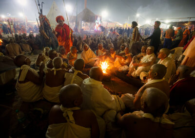 A group of Naga Sadhvis also called “Maata” are sitting in front of a fire during a mass initiation ceremony. In the community of Naga Sadhus, both men and women are present. However, female Naga Sadhus are rare and seldom interact with the world. Women become Naga Sadhus after rigorous penance. For this, they have to perform the same rigorous reparation for years, offer Pind Daan while they are still alive, shave their heads, and then go somewhere and become a female Naga Sadhu. Female Naga Sadhus live secluded lives in forests, caves, and mountains, dedicating themselves to the worship of God. Unlike male Naga Sadhus, female Naga Sadhus do not practice nudity; instead, they wear saffron-colored clothes. They live like other Naga Sadhus, but instead of remaining without clothes, they also wear saffron-colored clothes. The cloth worn by female Naga Sadhus is unstitched and used to cover their bodies. Female Naga Sadhus are also known for their strict adherence to celibacy and ascetic practices, just like their male counterparts. Despite the challenges they face, these women continue to pursue spiritual enlightenment and dedicate their lives to serving a higher purpose.