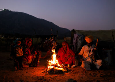 Banjara family sitting around a bonfire at night during Pushkar Mela in Rajasthan, India, faces lit by firelight.